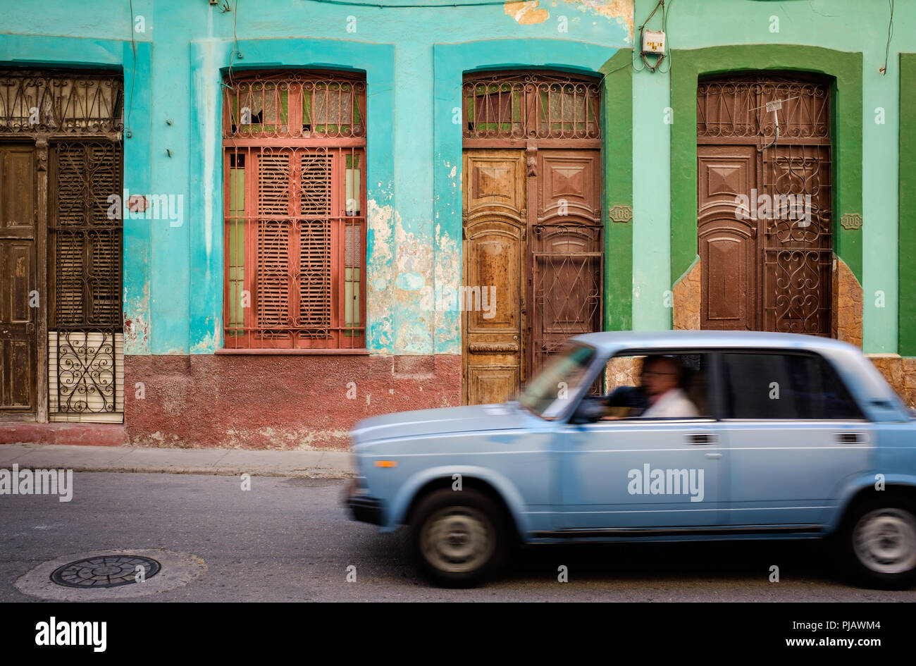 HAVANA, CUBA - CIRCA MARCH 2017: Old car drives in the streets of Havana, passing by a colorful home. Stock Photo