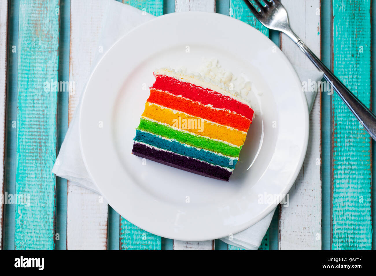 Rainbow cake on a white plate. Colorful wooden background. Top view. Stock Photo