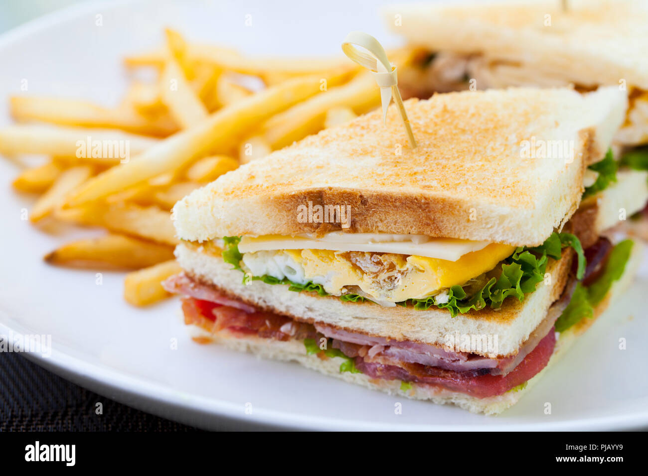 Club sandwich with french fries on a white plate. Close up. Stock Photo