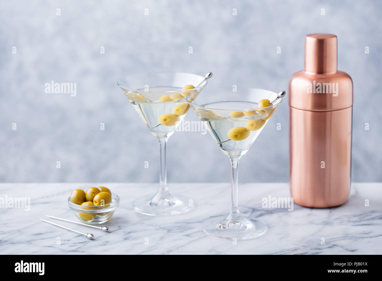 Martini cocktail with olives and bar shaker on marble table background