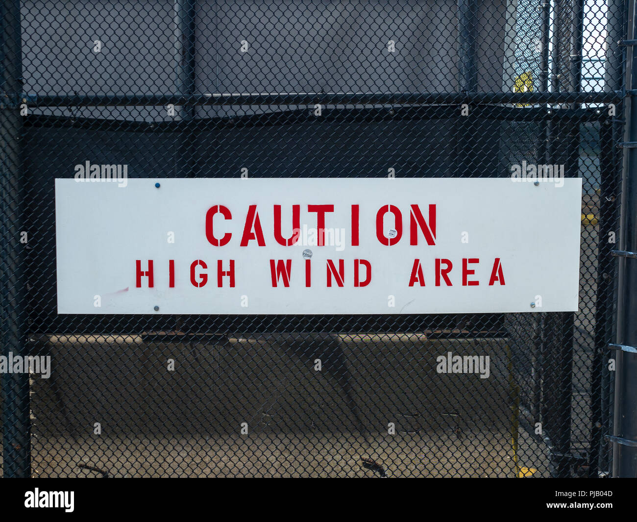 Caution high wind area sign handing on black fence  Stock Photo