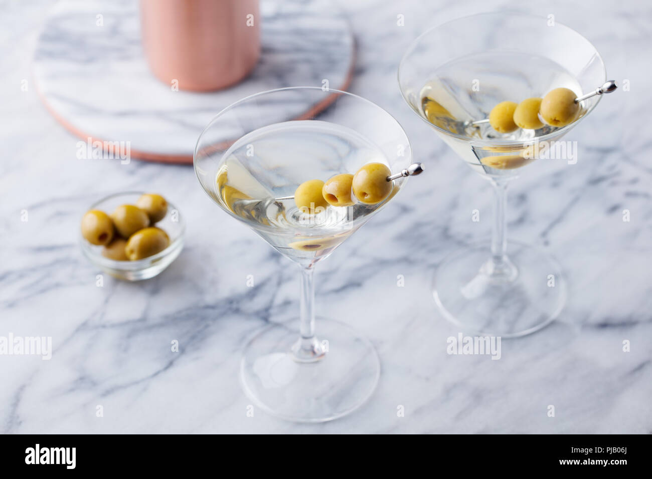 Martini cocktail with olives and bar shaker on marble table background