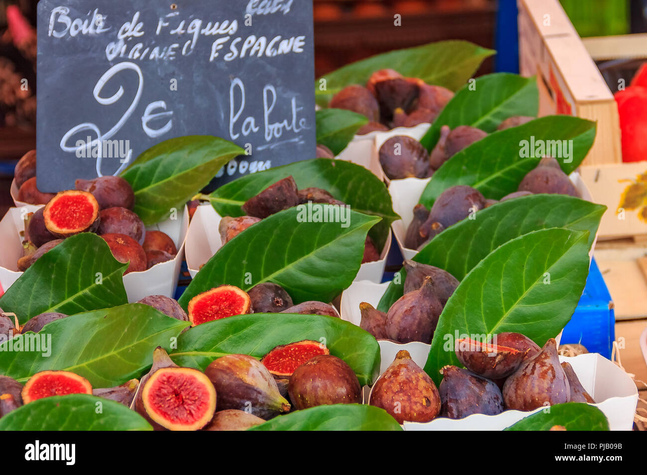 Ripe Mediterranean purple figs for sale with a handwritten chalkboard sign 'Box of figs from Spain 2 Euro' at a local outdoor farmers market in Nice,  Stock Photo