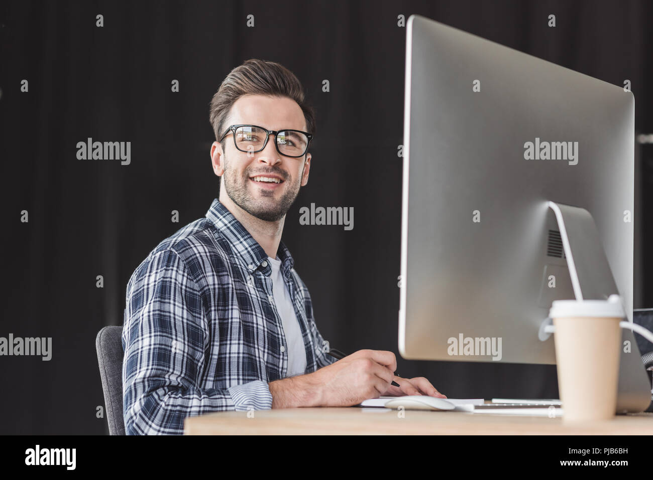 handsome smiling young programmer in eyeglasses working with desktop computer Stock Photo