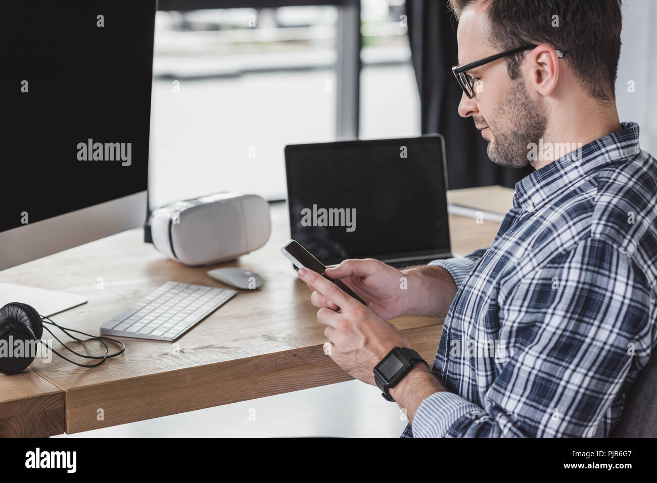 handsome young programmer in eyeglasses using smartphone at workplace Stock Photo