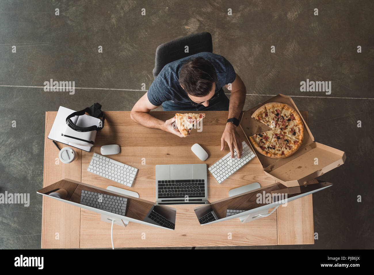 overhead view of programmer eating pizza and using computers at workplace Stock Photo