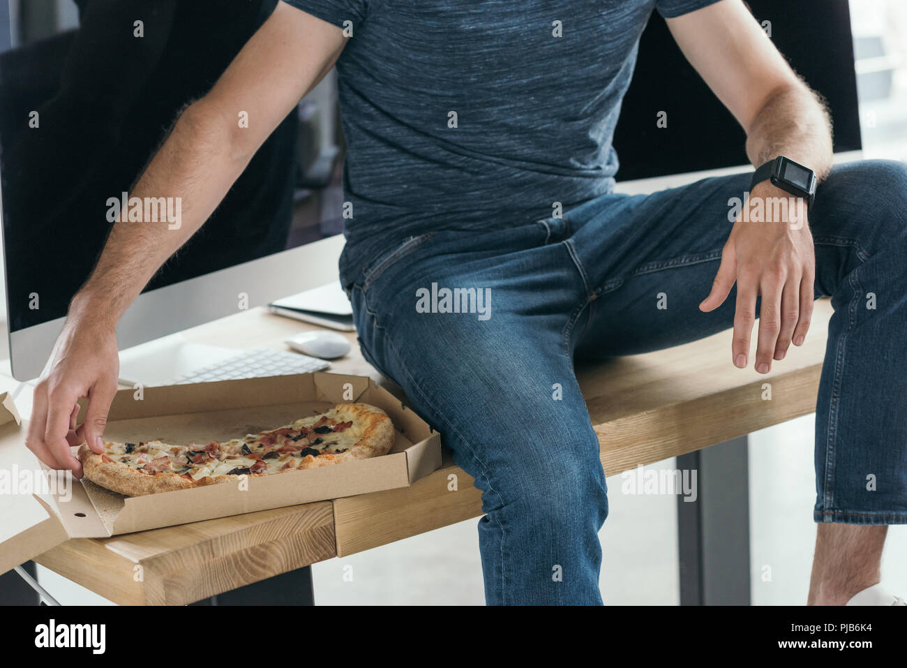 cropped shot of young programmer eating pizza at workplace Stock Photo