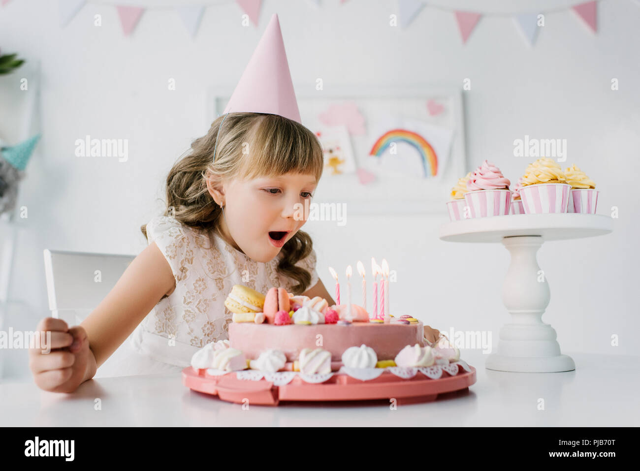 little birthday girl in cone blowing out candles from cake on table Stock Photo Alamy