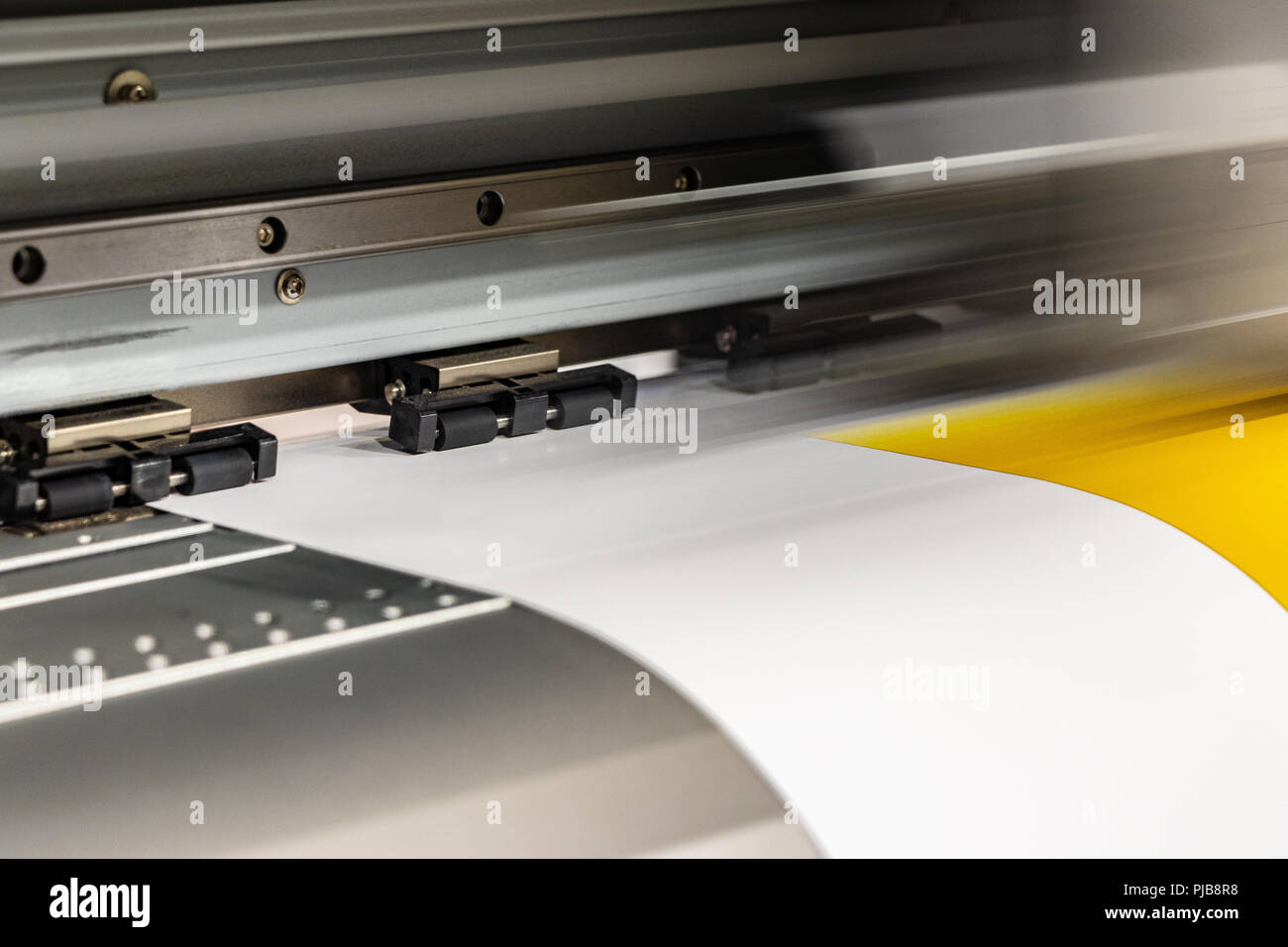 Detail of big print head passing on yellow glossy paper rolls. Stock Photo