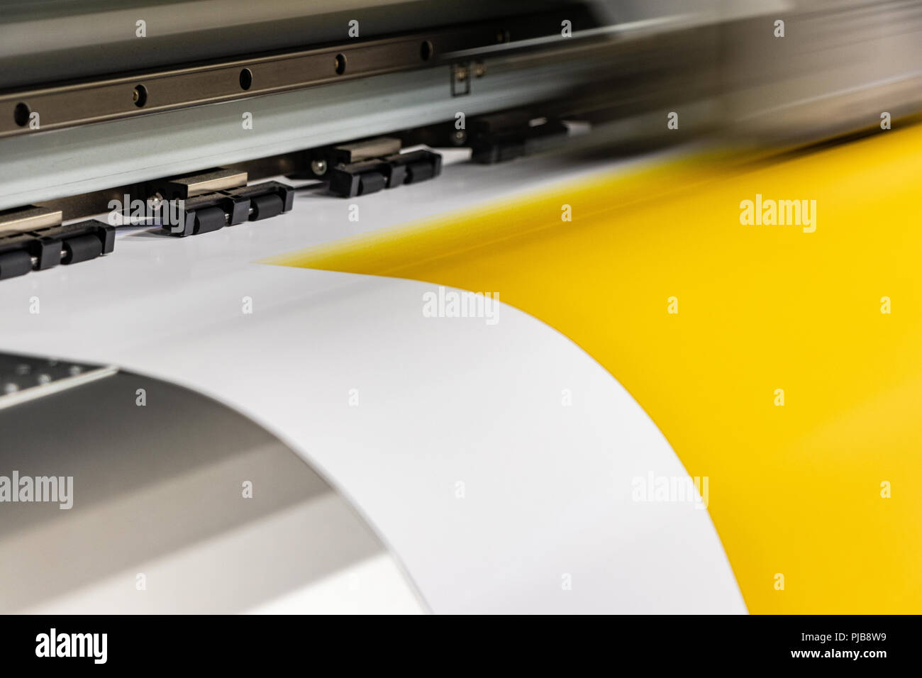 Detail of big print head passing on yellow glossy paper rolls. Stock Photo