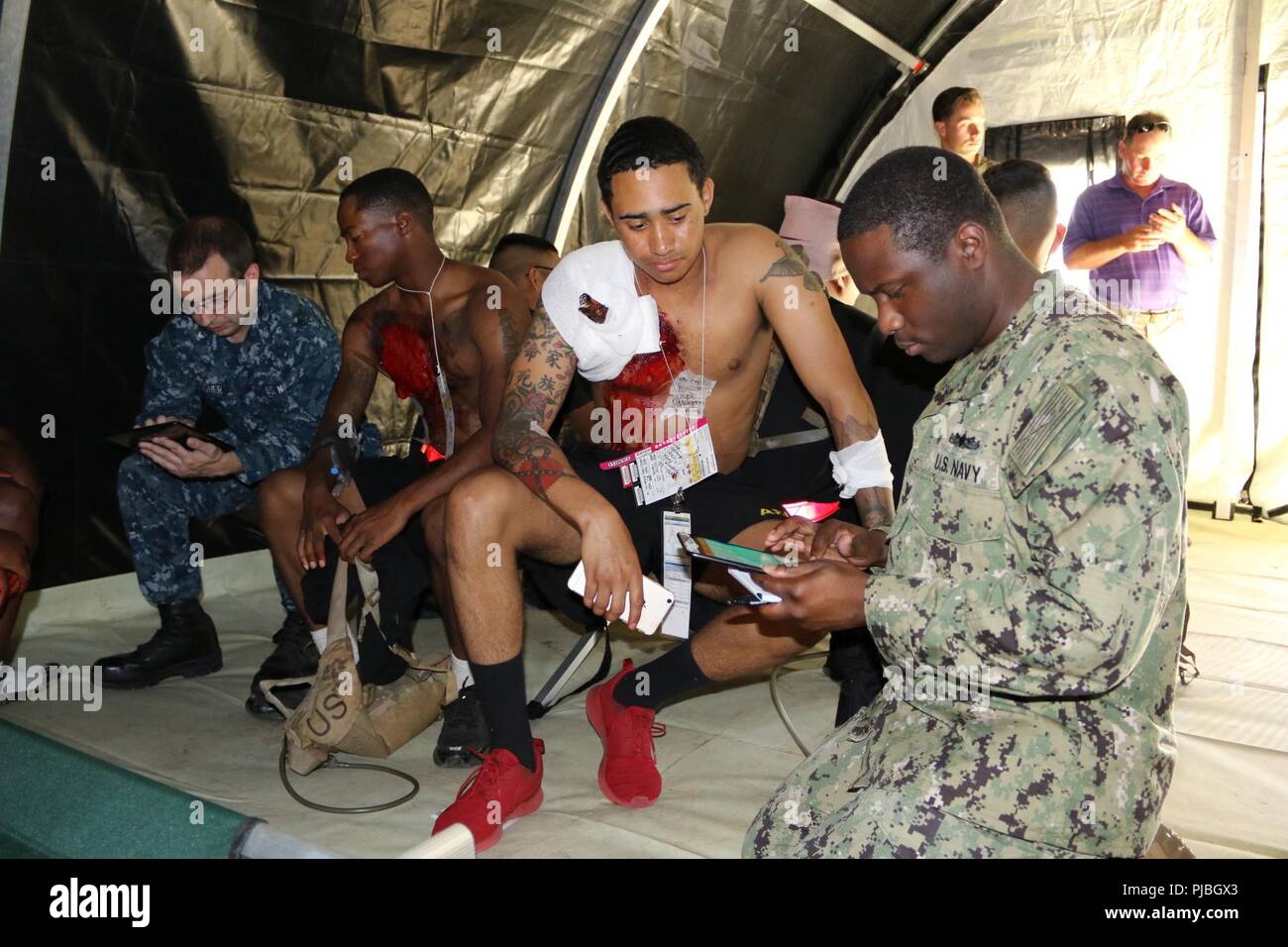 JOINT BASE PEARL HARBOR-HICKAM, Hawaii (July, 12, 2018) U.S. Army Spc. Jaylen Jones, 84th Engineer Batallion Soldier and patient actor, sports a mock impalement while providing simulated medical information to Petty Officer 2nd Class James Farrington III, a corpsman at the Naval Health Clinic Hawaii, who is testing out a new electronic medical record system designed to virtually document medical encounters in the field environment. The mock scenario is part of the U.S. Navy’s Rim of the Pacific exercise, as part of the humanitarian assistance and disaster relief portion of the training event.  Stock Photo
