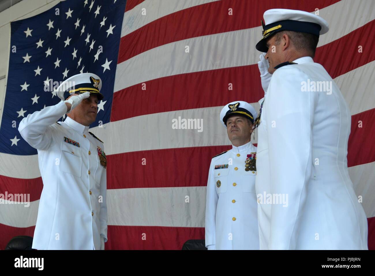 Capt. Andrew W. Ericks (left) relieves Capt. Frederick C. Riedlin (right) as commanding officer of Air Station Barbers Point while Rear Adm. Brian Penoyer (center) observes at a change of command ceremony at Air Station Barbers Point, July 6, 2018. Riedlin is transferring to become the Chief of the Office of Aviation Forces (CG-711). Stock Photo