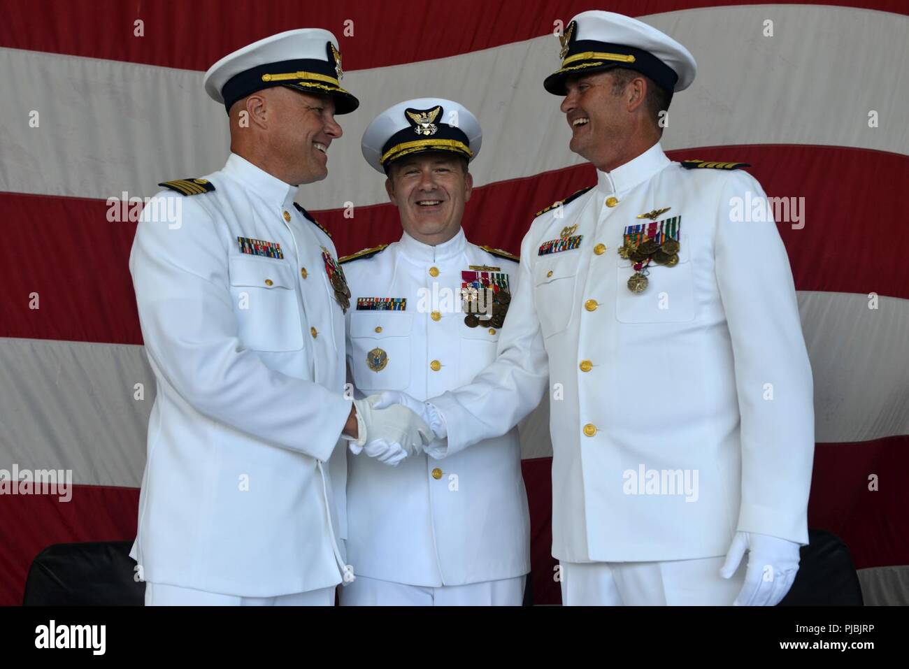 Capt. Andrew W. Eriks (left) shakes hands with Capt. Frederick C. Riedlin (right) while Rear Adm. Brian Penoyer (center) looks on at a change of command ceremony at Air Station Barbers Point, July 6, 2018. Coast Guard aviation has been present at Barbers Point since 1949 and officially designated as Coast Guard Air Station Barbers Point in 1965. Stock Photo