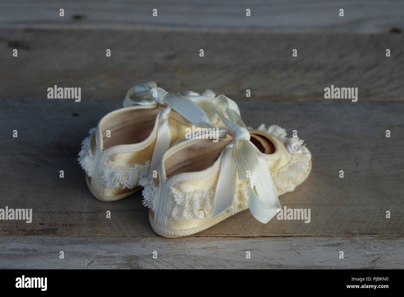 vintage baby shoes tied with ruffles and little flowers close up on a natural wooden background Stock Photo