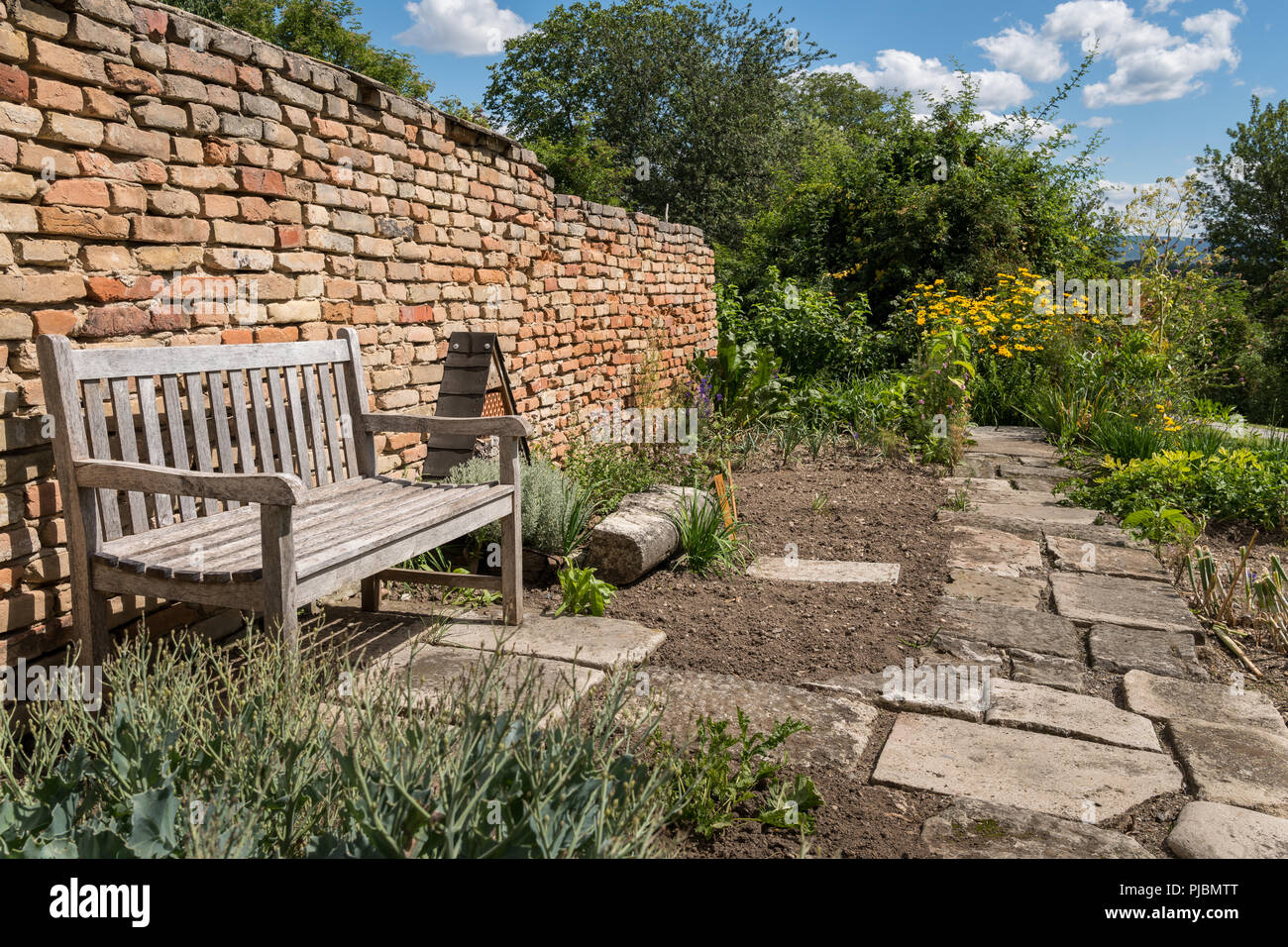 A wooden bench standing in front of a brick wall in a garden Stock ...