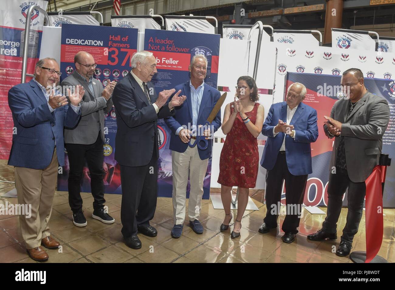 (July 16, 2018) George Brett, National Baseball Hall of Famer, center, former Secretary of the Navy, the Honorable John H. Dalton, left, and members of the Bob Feller Act of Valor Foundation, cut a ribbon during a ceremony for the Bob Feller Act of Valor Foundation's launch of its traveling educational exhibit at the National Museum of the United States Navy (NMUSN). The traveling exhibit is displayed in the NMUSN and is alongside the museum's recently opened exhibit, 'Playball - Navy and the National Pastime,' which highlights the history of baseball and the U.S. Navy. Stock Photo
