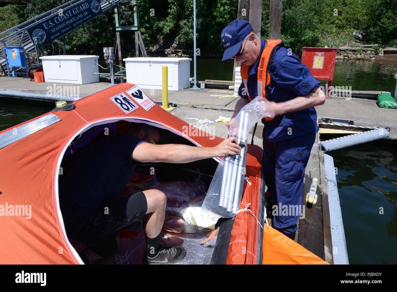 Ron Hilburger, a Coast Guard Auxiliary sector coordinator, assists in the unpacking of survival equipment from an inflatable life raft to showcase for members of the Washington Homeland Security Roundtable at Marine Safety Unit Portland, Ore., July 16, 2018.    The Coast Guard Auxiliary is an all-volunteer organization that acts as a mobile force-multiplier for the Coast Guard's many missions.    U.S. Coast Guard Stock Photo