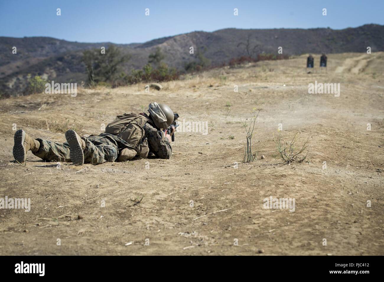 U.S. Marine Corps Pfc. Mathew Garcia, student, 2nd platoon, Hotel Company, Marine Combat Training Battalion, shoots at a target on Range 219 with a M16A4 service rifle at Marine Corps Base Camp Pendleton, California, July 13, 2018. The Marines shot live ammunition during their buddy rush exercise, which consisted of five Marines firing at the enemy while the other five ran ahead. Stock Photo