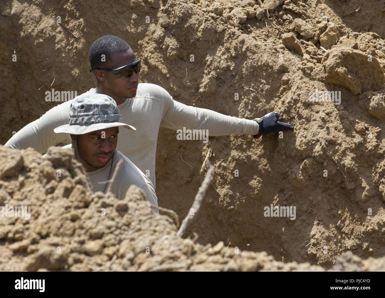 U.S. Air Force Senior Airman Aaron Lister, top, and Staff Sgt. Marlon Jackson, both with the 166th Civil Engineer Squadron, Delaware Air National Guard, observe from inside a hole the removal of dirt for the placement of a concrete storm water pipe, as part of phase one construction of Camp Kamassa in Crystal Springs, Mississippi, July 12, 2018. Camp Kamassa will be the states first fully handicap accessible, year round camp facility for children and adults with special needs, that is being built on 326 acres spearheaded by the Department of Defense's Innovative Readiness Training program. Stock Photo