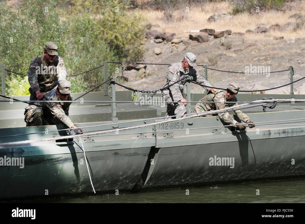 U.S. Army Soldiers from the California Army National Guard’s 132nd Multirole Bridge Company, 579th Engineer Battalion, 49th Military Police Brigade, secure tension cables that hold a floating bridge together July 13 at Cache Creek Regional Park, California. The 132nd erected a 100-foot temporary bridge to support heavy trucks and emergency vehicles battling Northern California wildfires. Shown: U.S. Army Spcs. Christian Berg, Bryce F. Jones, Aaron W. Parker and Michael Fereira. Stock Photo