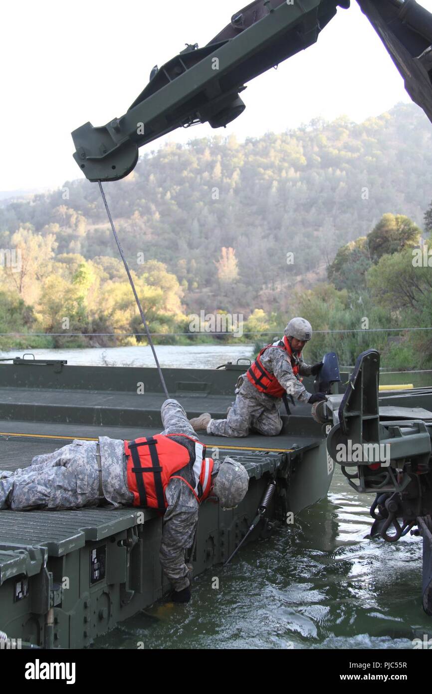 Members of the 132nd Multirole Bridge Company (MRBC), 579th Engineer Battalion, 49th Military Police Brigade, California Army National Guard, “buddy up” to secure a steel cable Aug. 7, 2015 at Cache Creek Regional Park in Yolo County, California. The Redding, California unit was called again (July 2018) to assist the ongoing wildfires in northern California by erecting a temporary floating bridge that will grant CAL FIRE easier access to battle the blazes. Stock Photo
