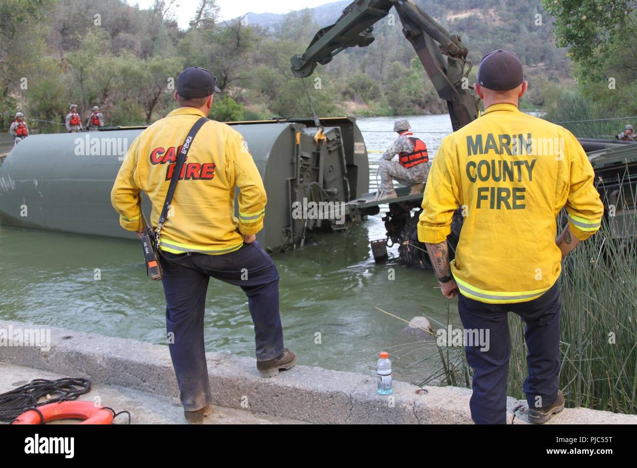 California Department of Forestry and Fire Protection (CAL FIRE) personnel assigned to the 2015 Rocky Fire in Northern California watch as the California Army National Guard’s 132nd Multirole Bridge Company (MRBC), 579th Engineer Battalion, 49th Military Police Brigade, from Redding, California, place a “bay” into the Cache Creek River Aug. 7, 2015 at Cache Creek Regional Park in Yolo County, California. Representatives from CAL FIRE as well as other government agencies were on hand to watch the California National Guard unit perform its duty again in July 2018. Stock Photo