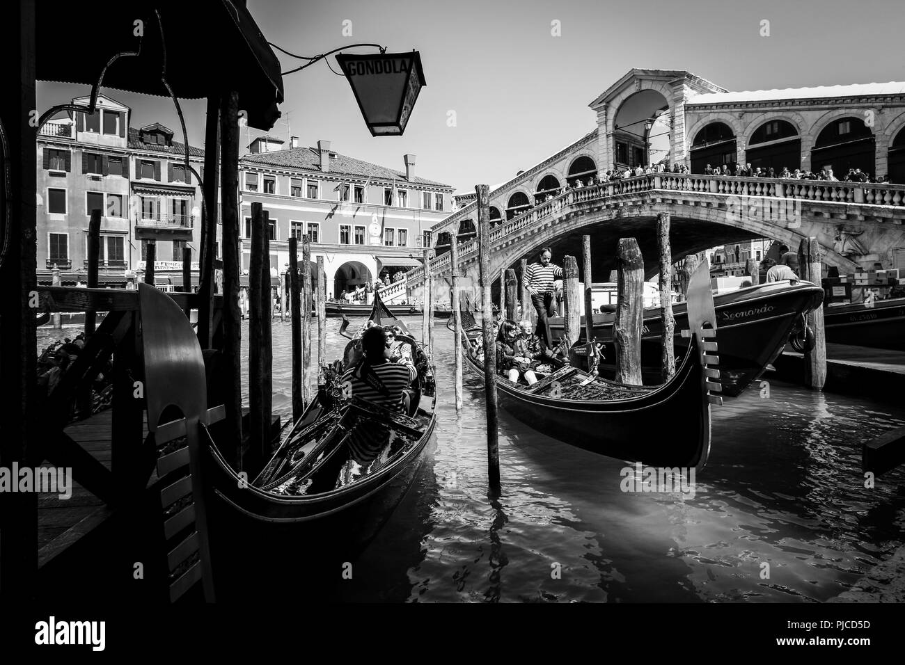 Two gondolas getting ready for a ride on the Grand Canal in Venice, while tourists watching the scene from the Rialto Bridge in the background Stock Photo