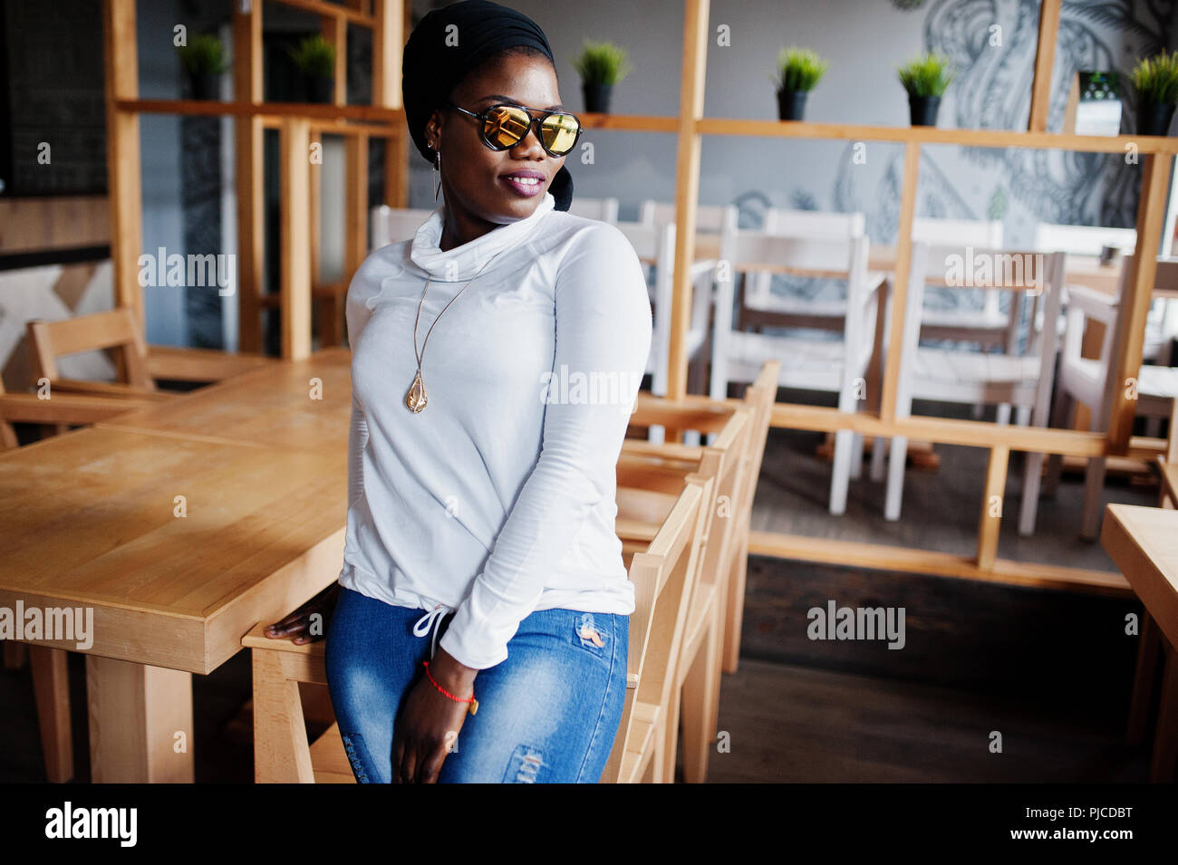 African muslim girl in black hijab and sunglasses posed at modern cafe . Stock Photo