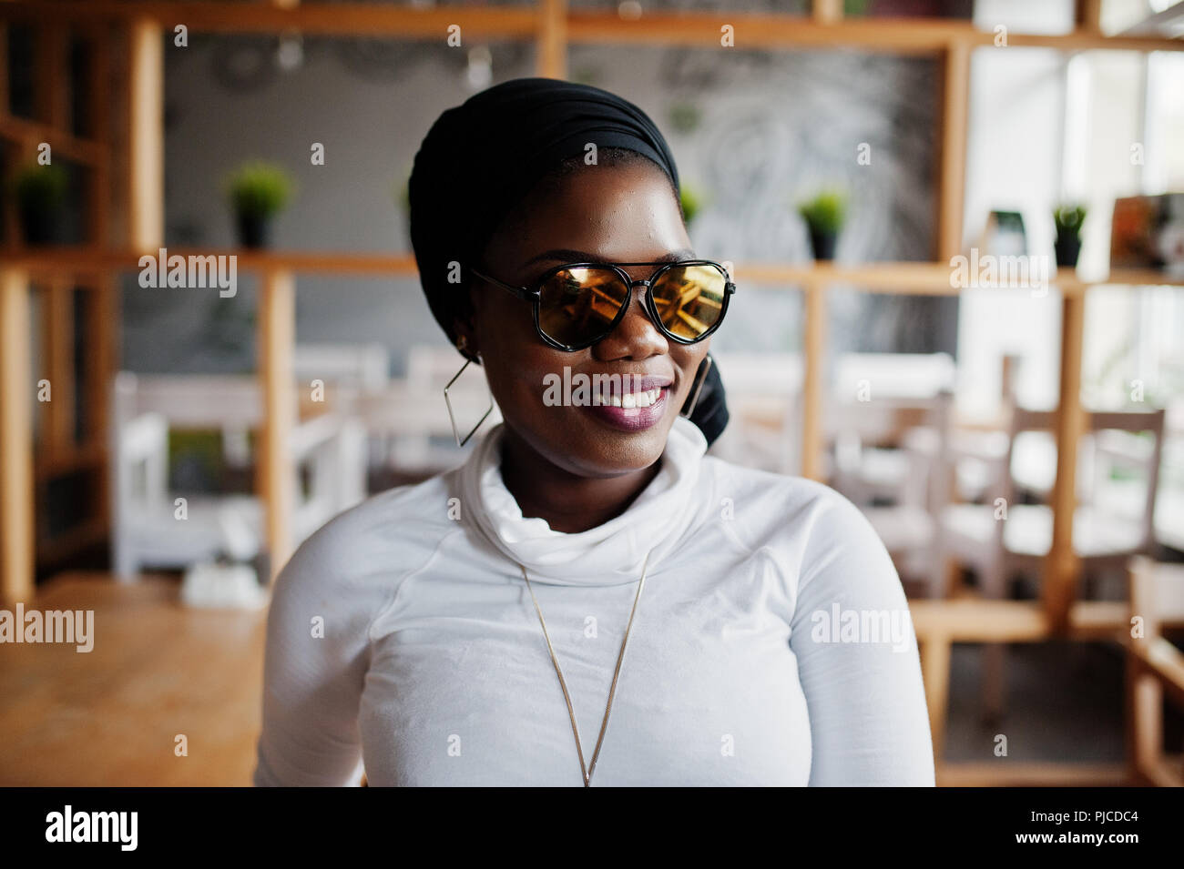 African muslim girl in black hijab and sunglasses posed at modern cafe . Stock Photo