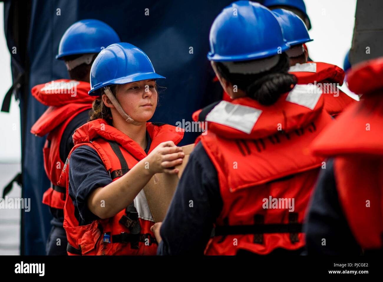 OCEAN (July 20, 2018) – Personnel Specialist 3rd Class Talia Toelle, from Des Moines, Iowa, passes a box of food aboard the guided-missile destroyer USS Dewey (DDG 105) during a connected replenishment. Dewey is underway in the U.S. 3rd Fleet area of operations. Stock Photo