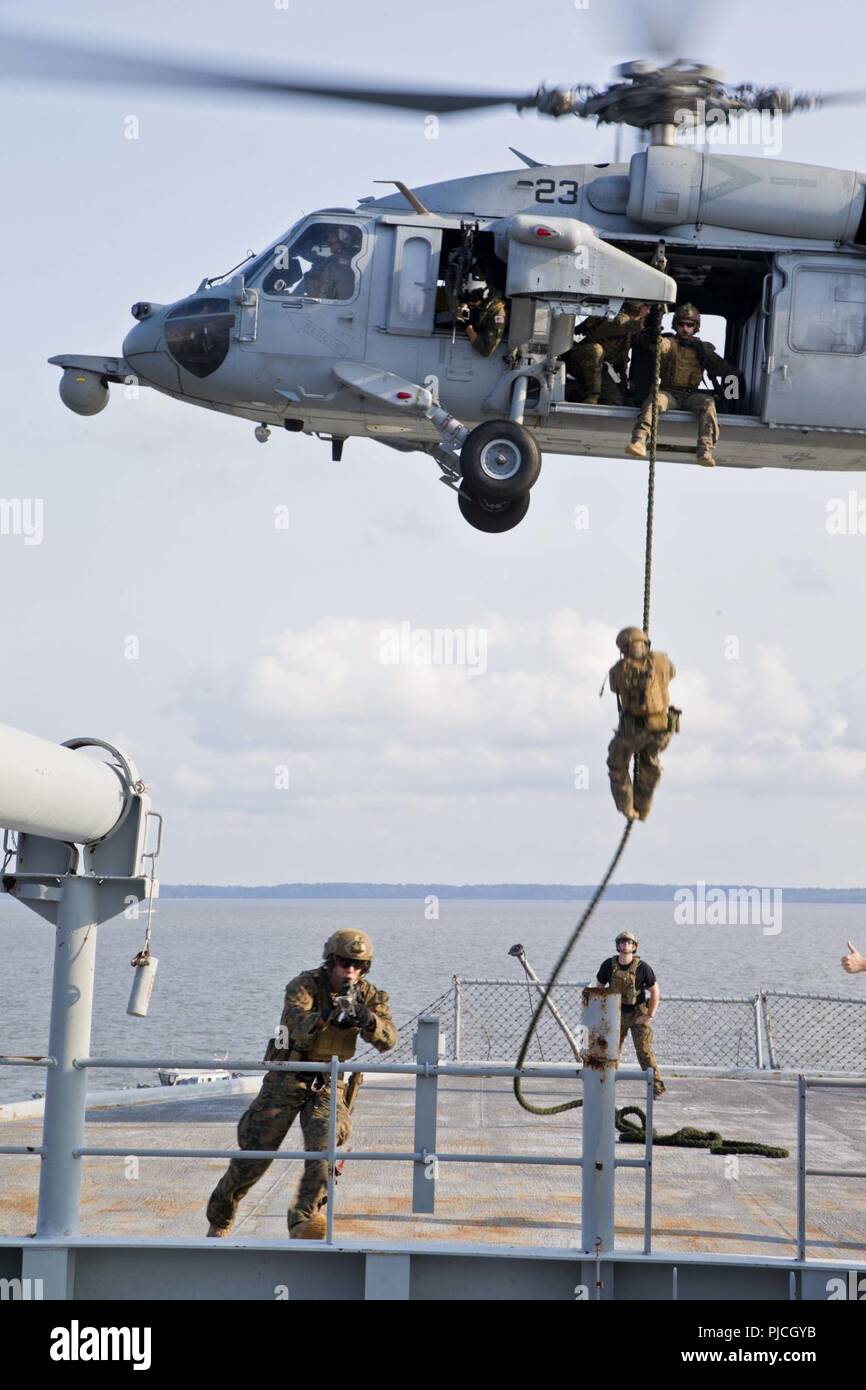 U.S. Marines with the Maritime Raid Force, 22nd Marine Expeditionary Unit, perform fast roping and security drills out of a MH-60 during a Visit, Board, Search and Seizure course at Fort Eustis, Virginia, July 12, 2018. This course gives the MRF the capability of launching VBSS operations during the 22nd MEU’s upcoming deployment. Stock Photo