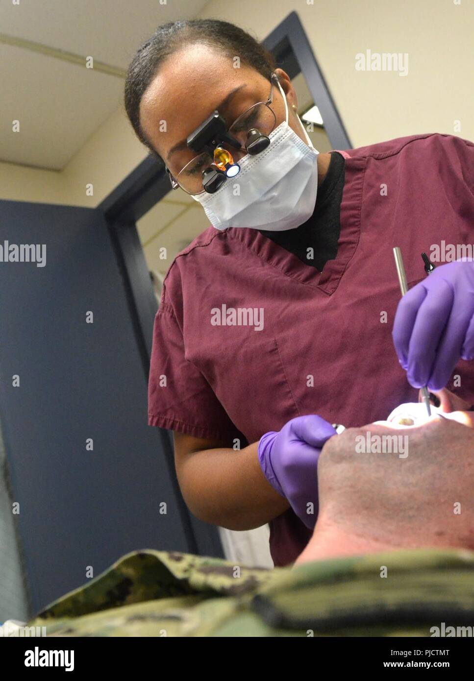JACKSONVILLE, Fla. (July 24, 2018) Lt. Cmdr. Charlie Cage, a dentist at Naval Branch Health Clinic Jacksonville, conducts an annual exam. Cage, a native of Dominica, British West Indies, says “The Dental Corps plays a vital role in mission readiness. We provide quality dental care which enables the military force to focus on their assigned tasks and it always begins with a dental exam. We always work as a team; a team of dentists, hygienists, assistants, and lab technicians.” The Dental Corps was established in 1912, and a few years later, had an immediate impact during World War I. Stock Photo