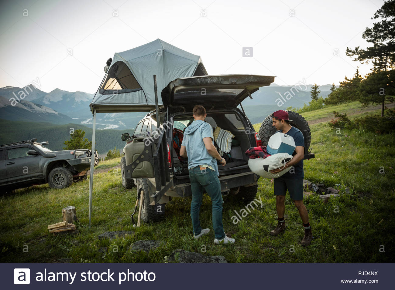 Friends camping, unloading SUV with rooftop tent in mountain field, Alberta, Canada Stock Photo
