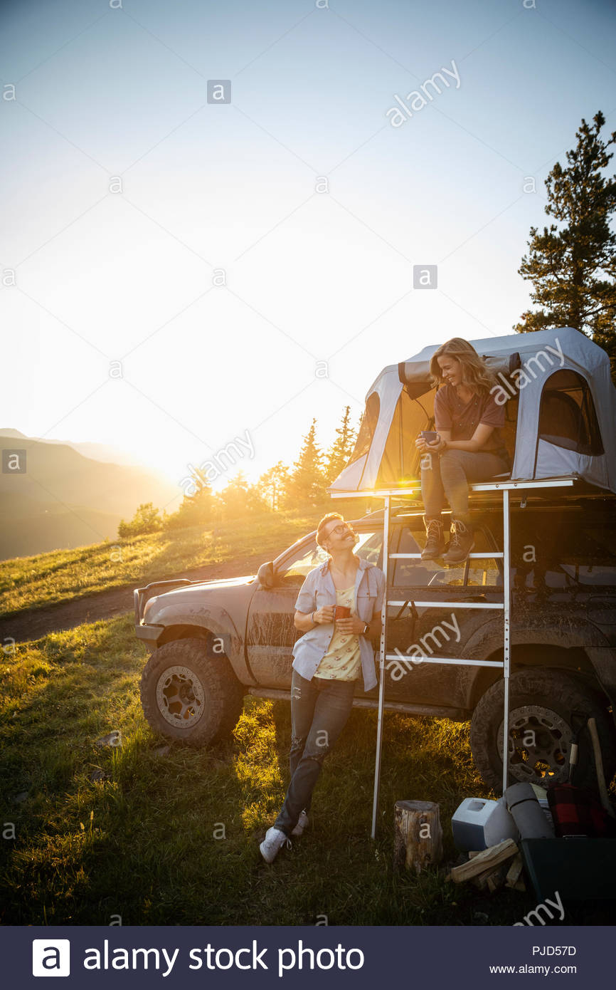 Couple camping, relaxing at SUV rooftop tent in sunny, idyllic field