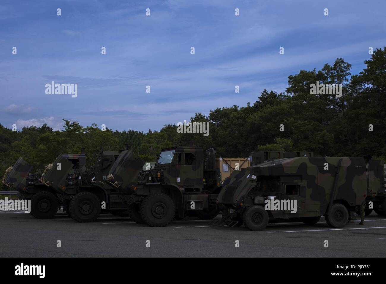 Tactical vehicles are parked with their hoods propped open during a convoy at a rest stop in Japan, July 13, 2018. The hoods are propped open at every rest stop during a convoy to cool off the engine. The convoy took service members with MWSS-171 to Combined Arms Training Center (CATC) Camp Fuji in order to begin exercise Eagle Wrath 18, an annual training exercise assessing the squadron’s combat readiness. Stock Photo