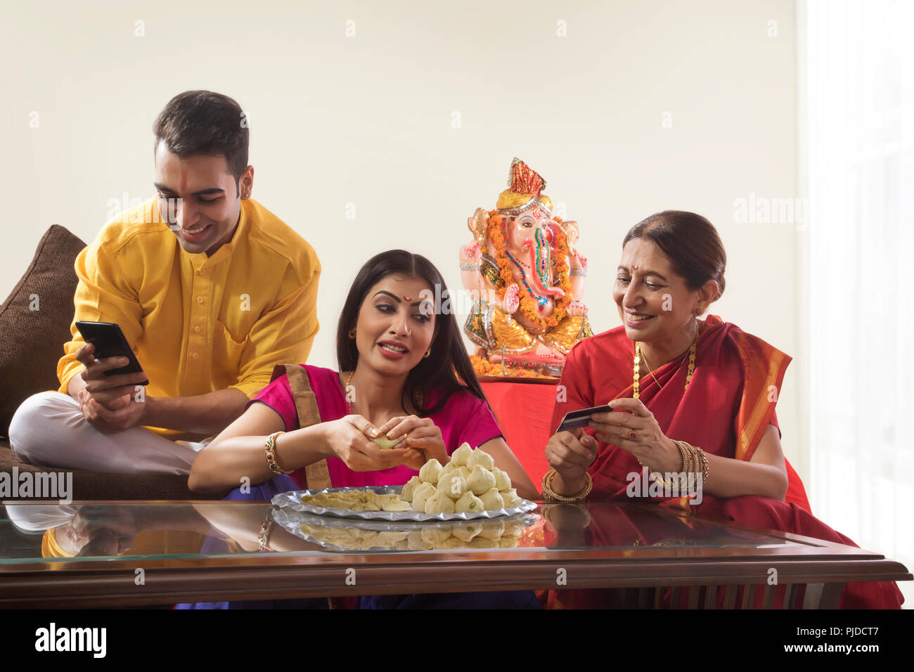 Husband wife sitting together while wife makes modaks and mother in law holds a credit card Stock Photo