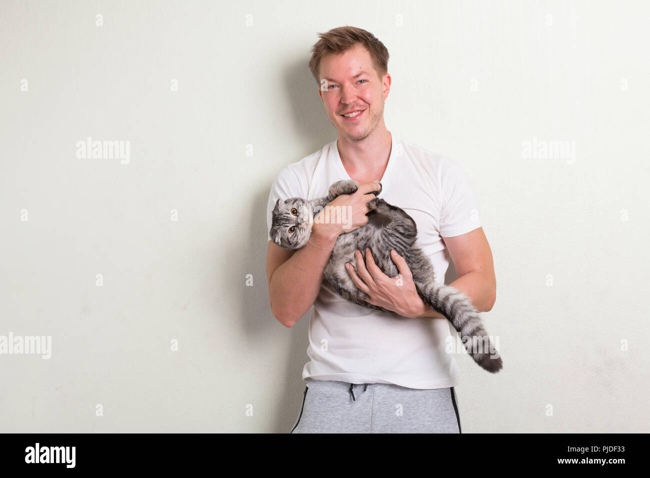 Young happy handsome man smiling while holding cute cat Stock Photo