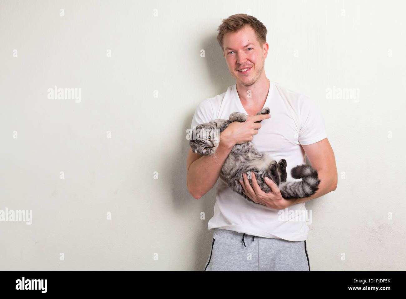 Young happy handsome man smiling while holding cute cat Stock Photo