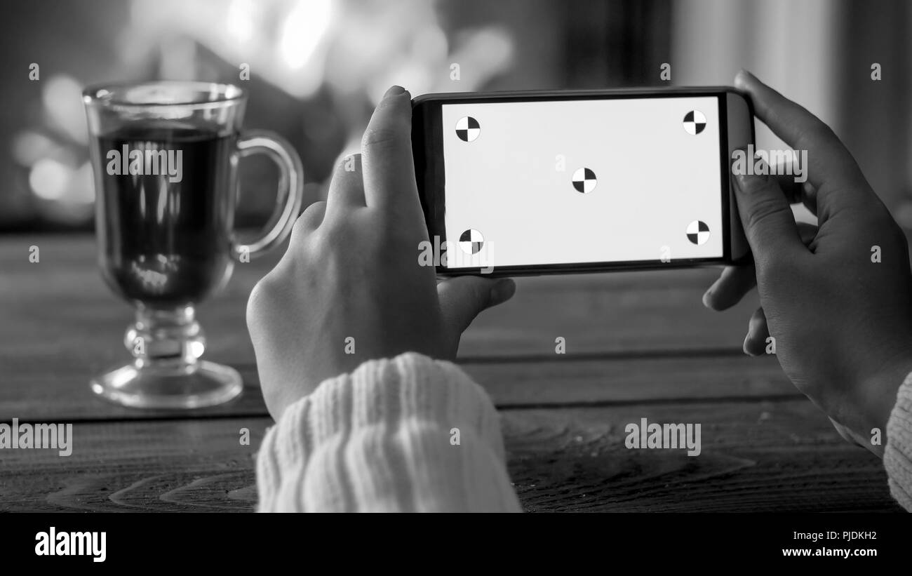 Black and white image of woman making photo of mulled wine in glass cup against burning fireplace. Empty screen for inserting your own picture or text Stock Photo
