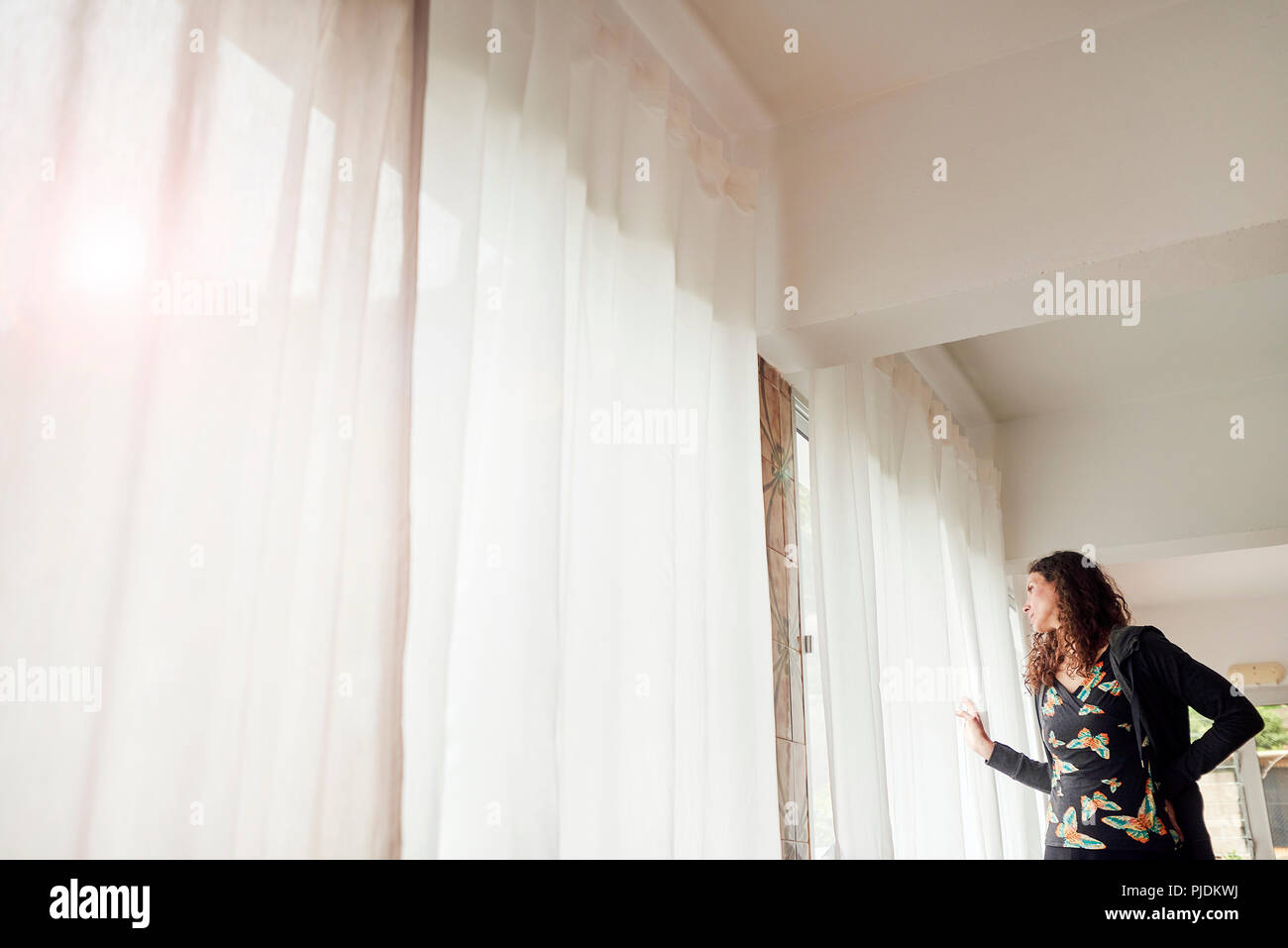 Woman peering out through net curtained window Stock Photo