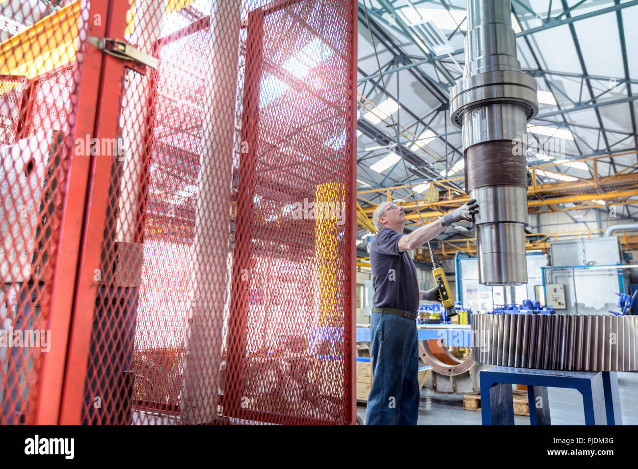 Engineer fitting spindle into heated gear wheel in gearbox factory Stock Photo