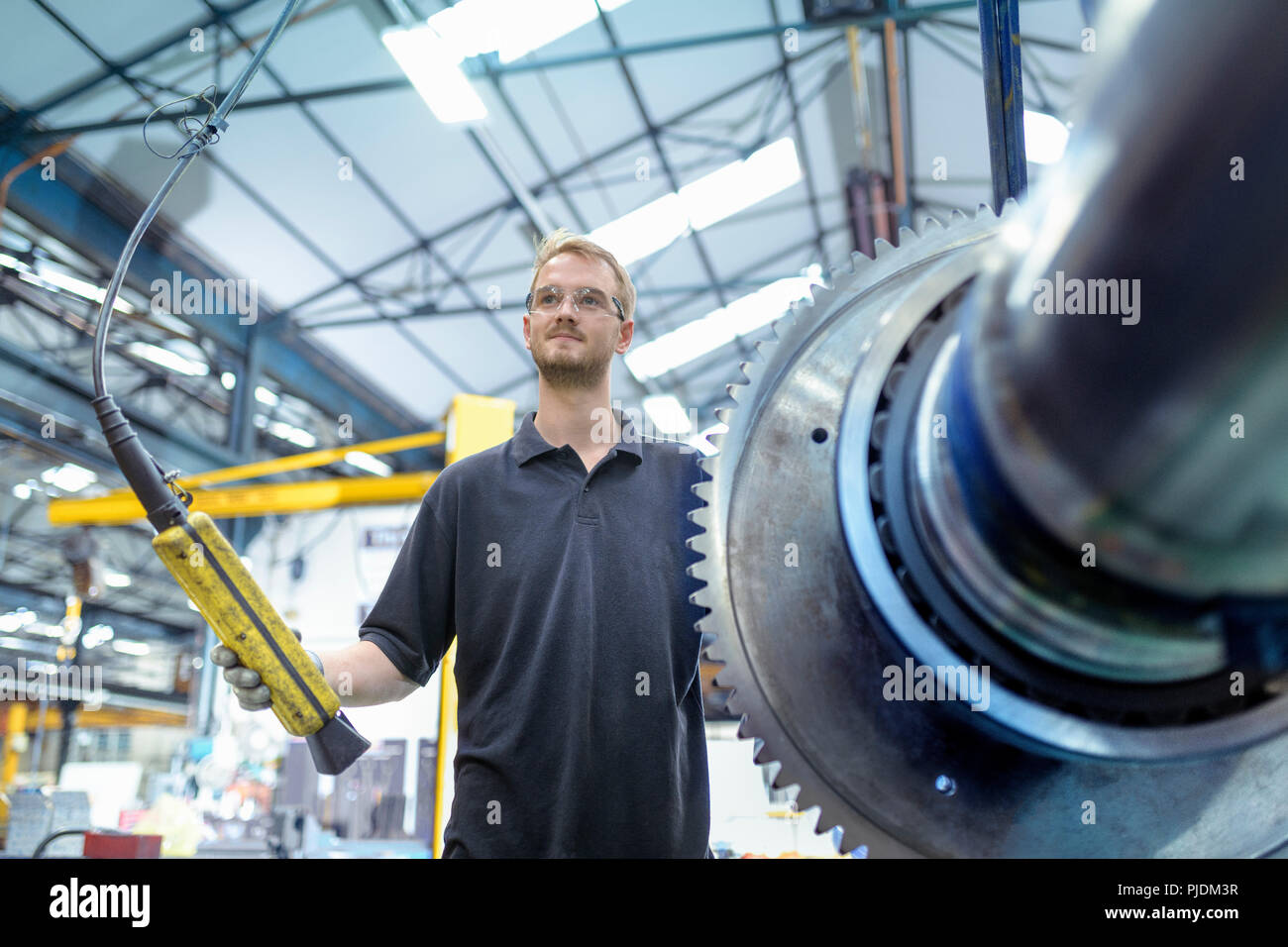 Portrait of engineer with crane and large gear in gearbox factory Stock Photo