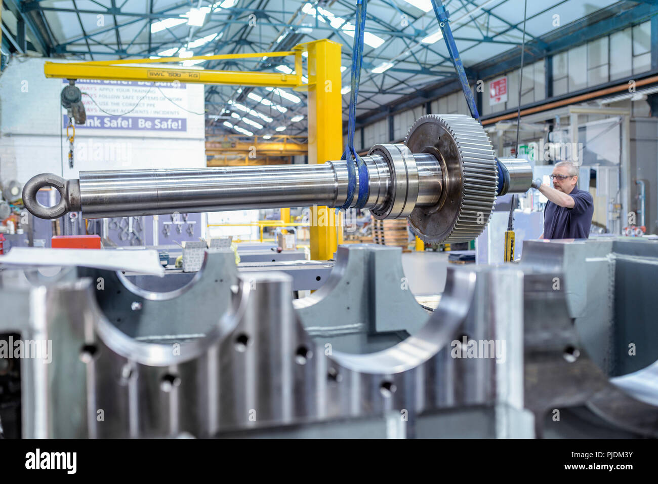 Engineer using crane to position large gear with spindle in gearbox factory Stock Photo