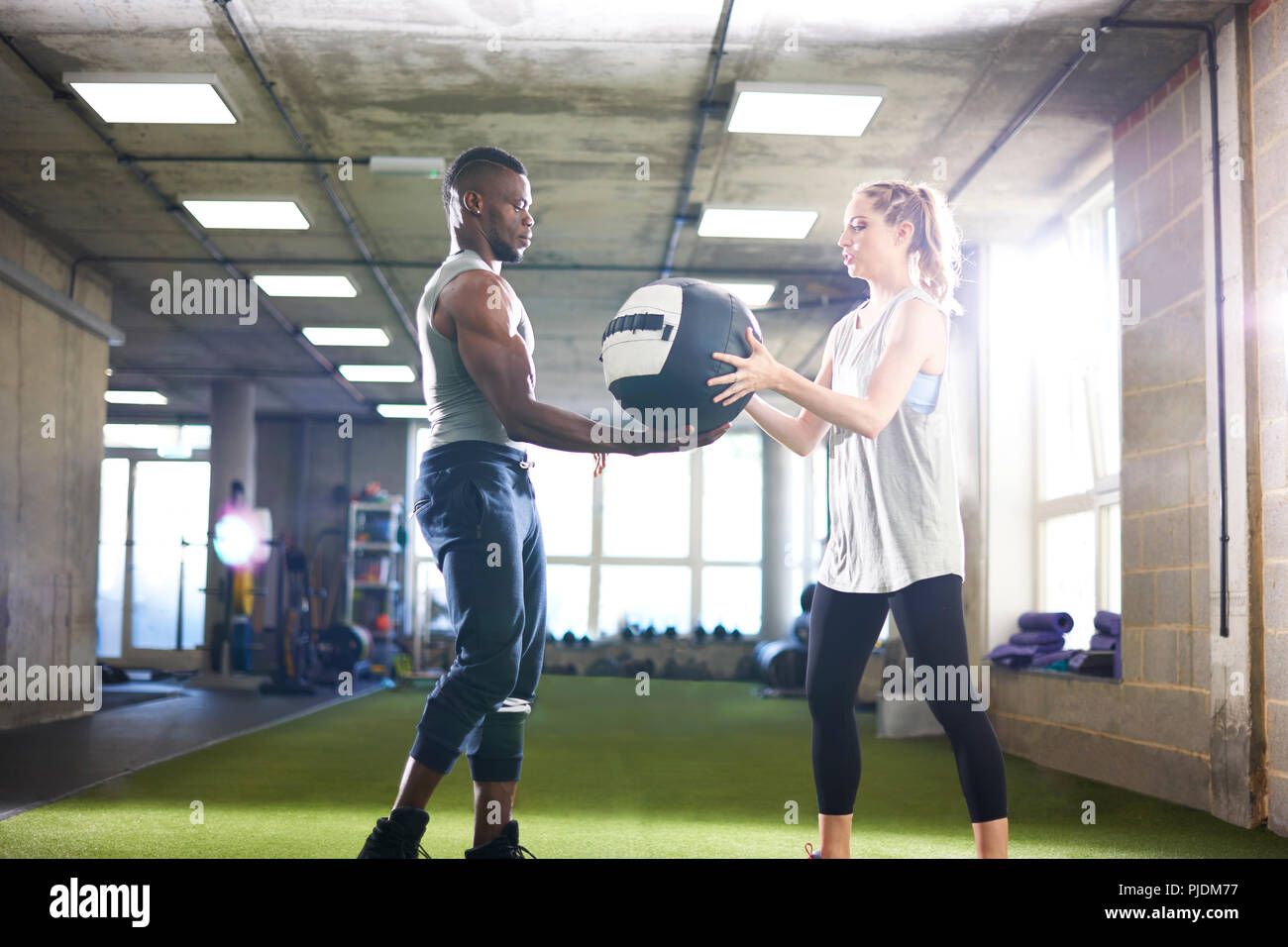 Trainer handing over medicine ball to female client in gym Stock Photo