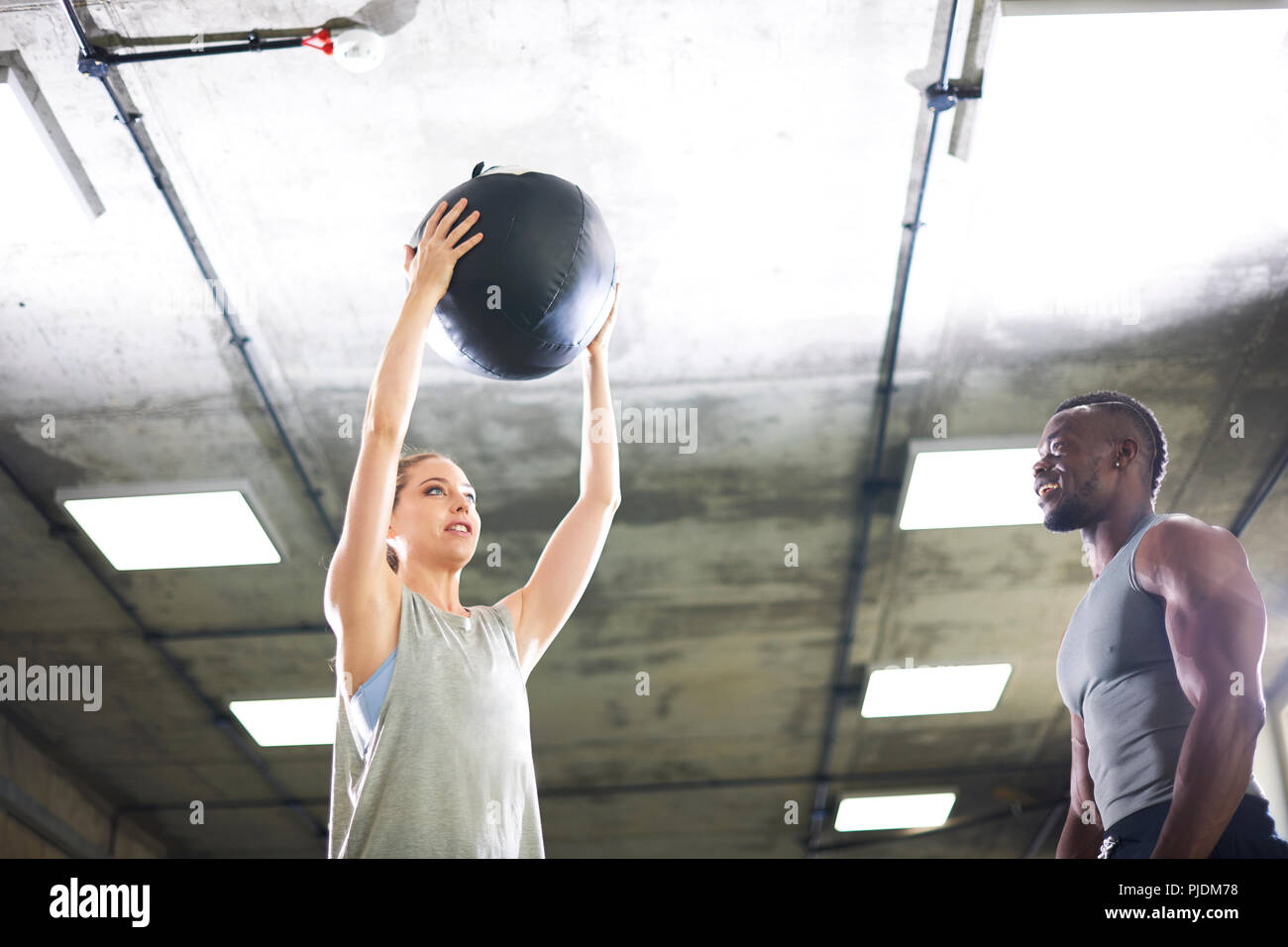 Trainer watching female client lift medicine ball in gym Stock Photo