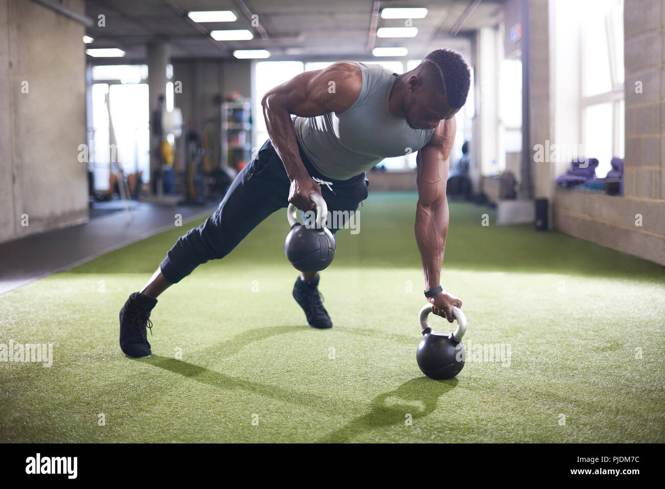 Man doing plank with kettlebells in gym Stock Photo