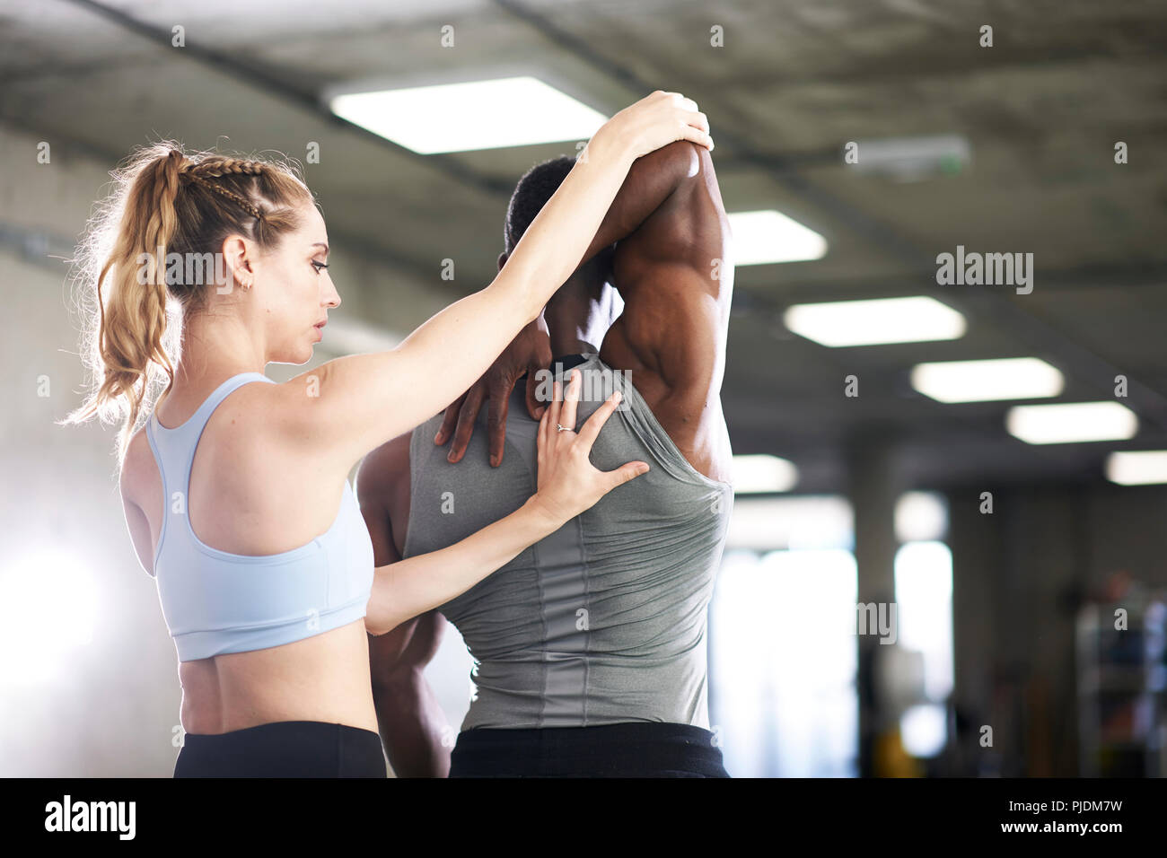 Trainer helping man with stretching exercise in gym Stock Photo