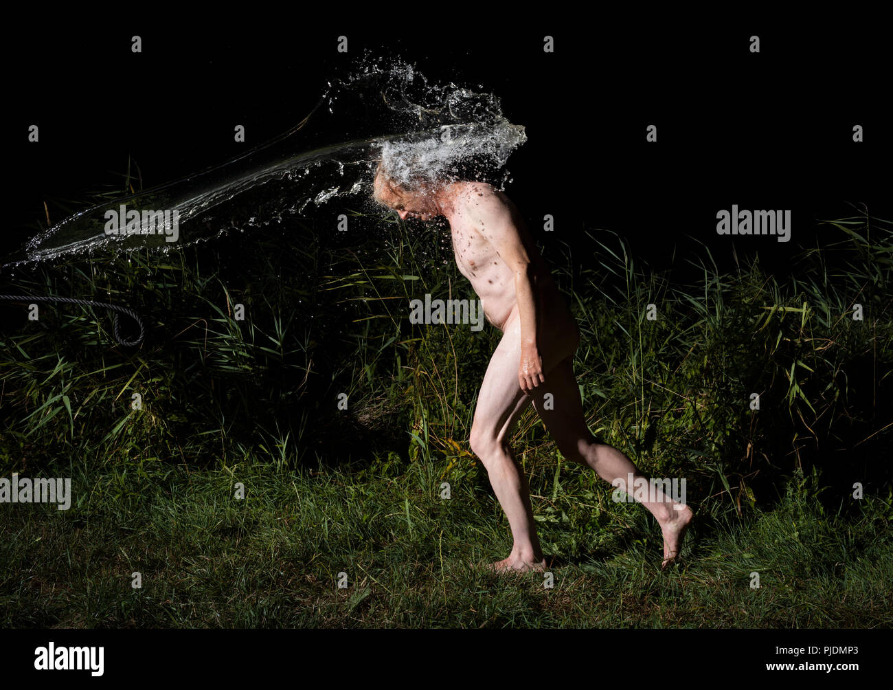Nude man gets water thrown at him on warm night Stock Photo