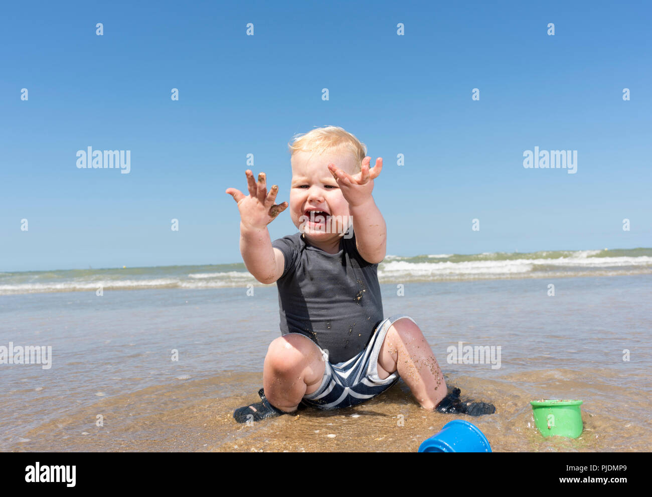 Toddler horrified with sea water on hands on beach Stock Photo