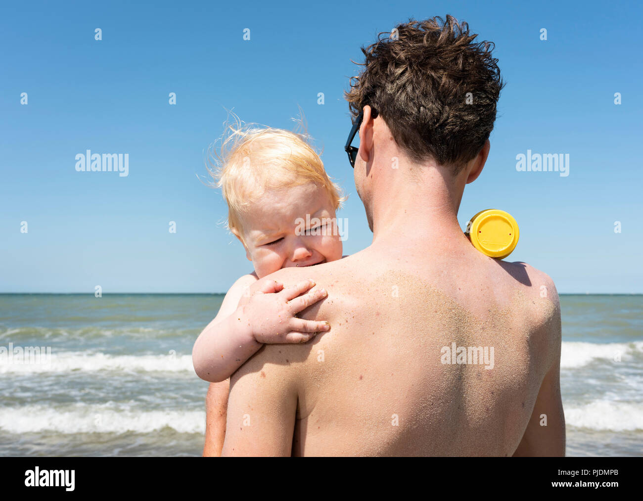 Toddler finds comfort with father on beach Stock Photo